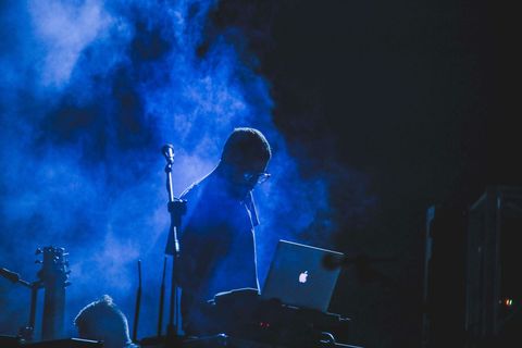 A musician at a laptop and microphone, lit in blue stage light