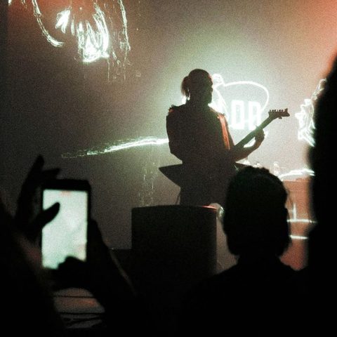 A fan in the crowd films a guitarist on stage with their phone