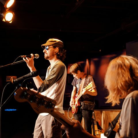 A singer in a cap and sunglasses at the mic, with a guitarist behind
