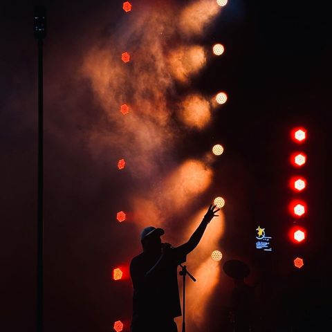 A singer in a cap, silhouetted against red stage lights and smoke